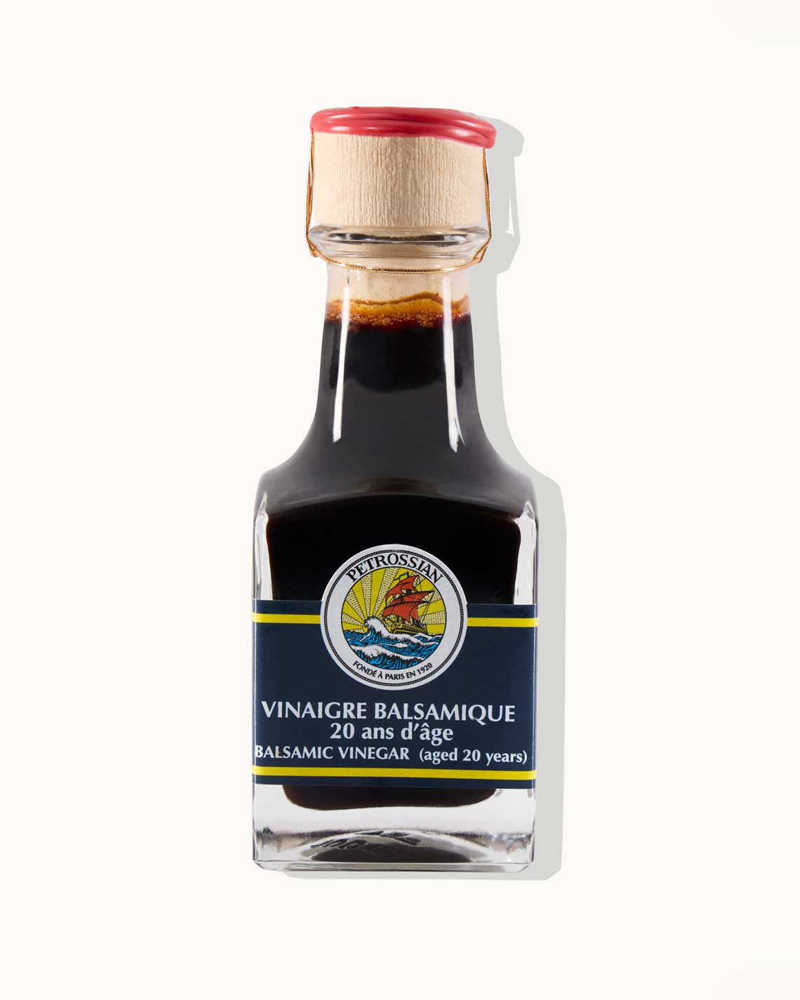 a glass bottle of dark, nearly black balsamic vinegar with a navy and yellow label, along with a cork and wax top, sits on a white background