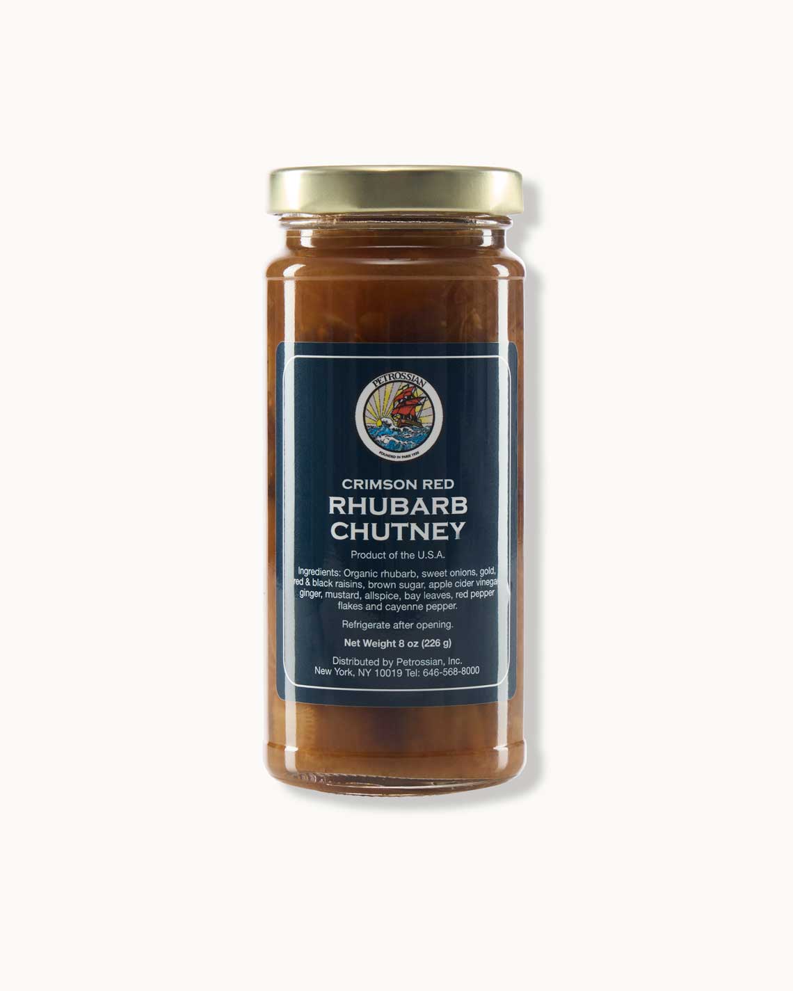 a glass jar with a copper lid and navy blue label filled with thick, red-brown chutney