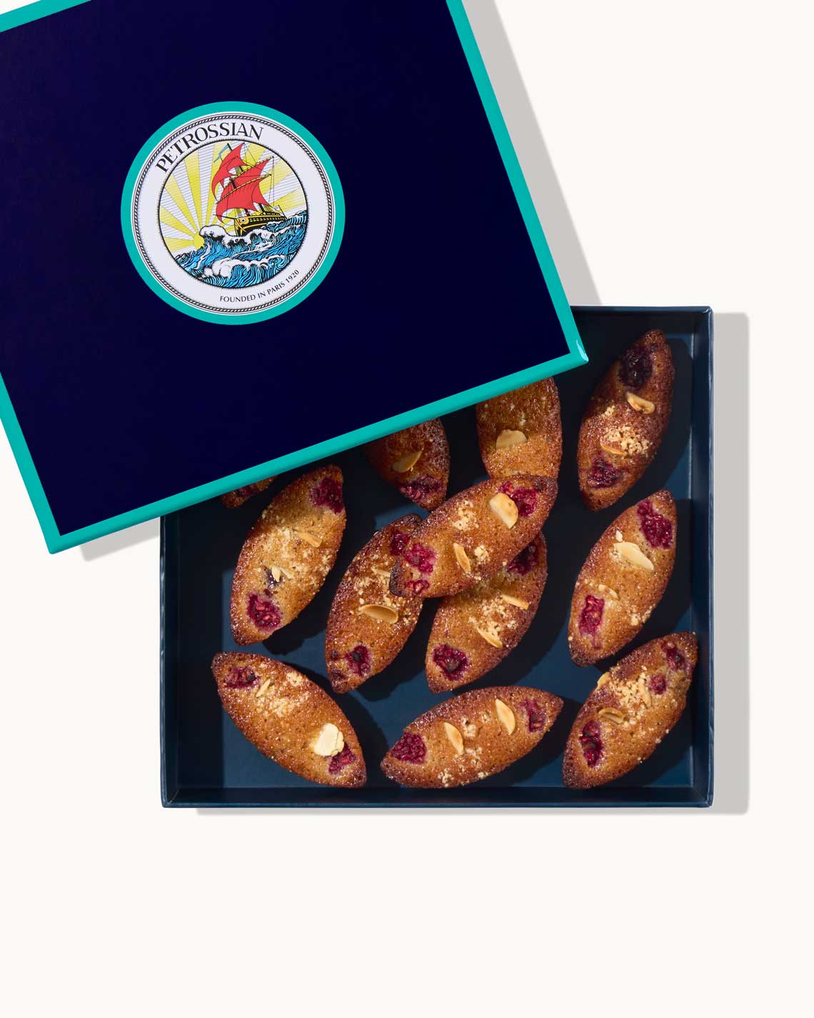 a navy blue Petrossian box with teal trim filled with golden brown financier cakes.