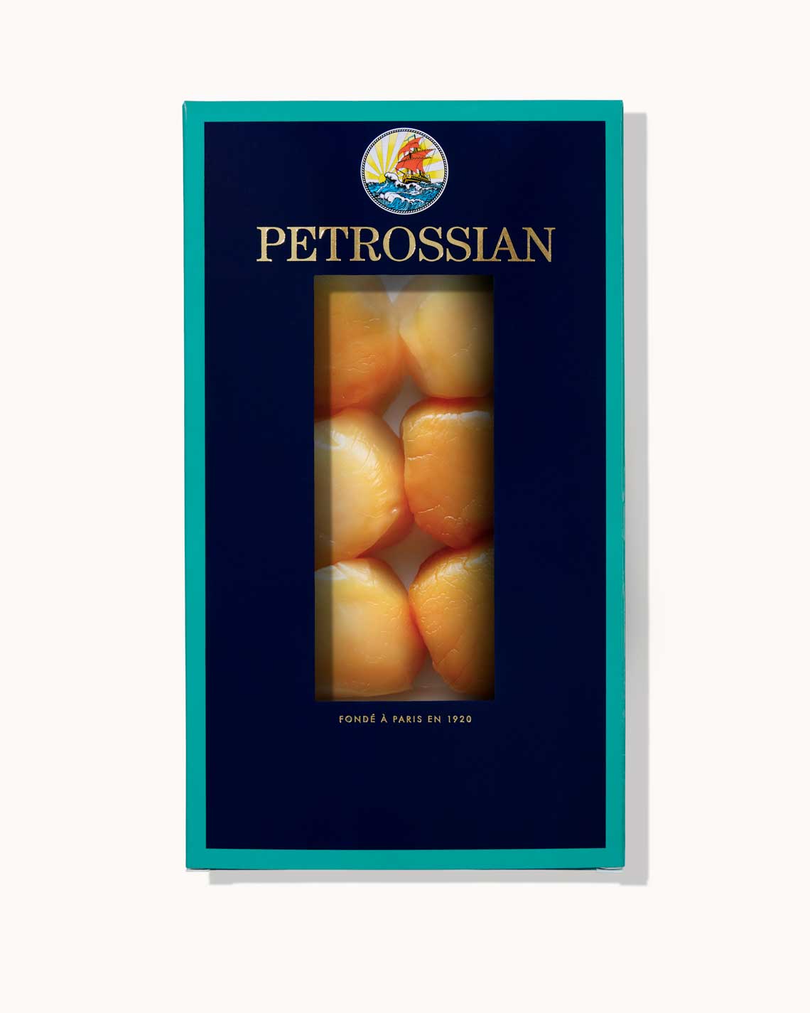 A navy blue Petrossian box with teal trim on a white background. Six large, thick diver's scallops can be seen through a cut-out in the center of the box.