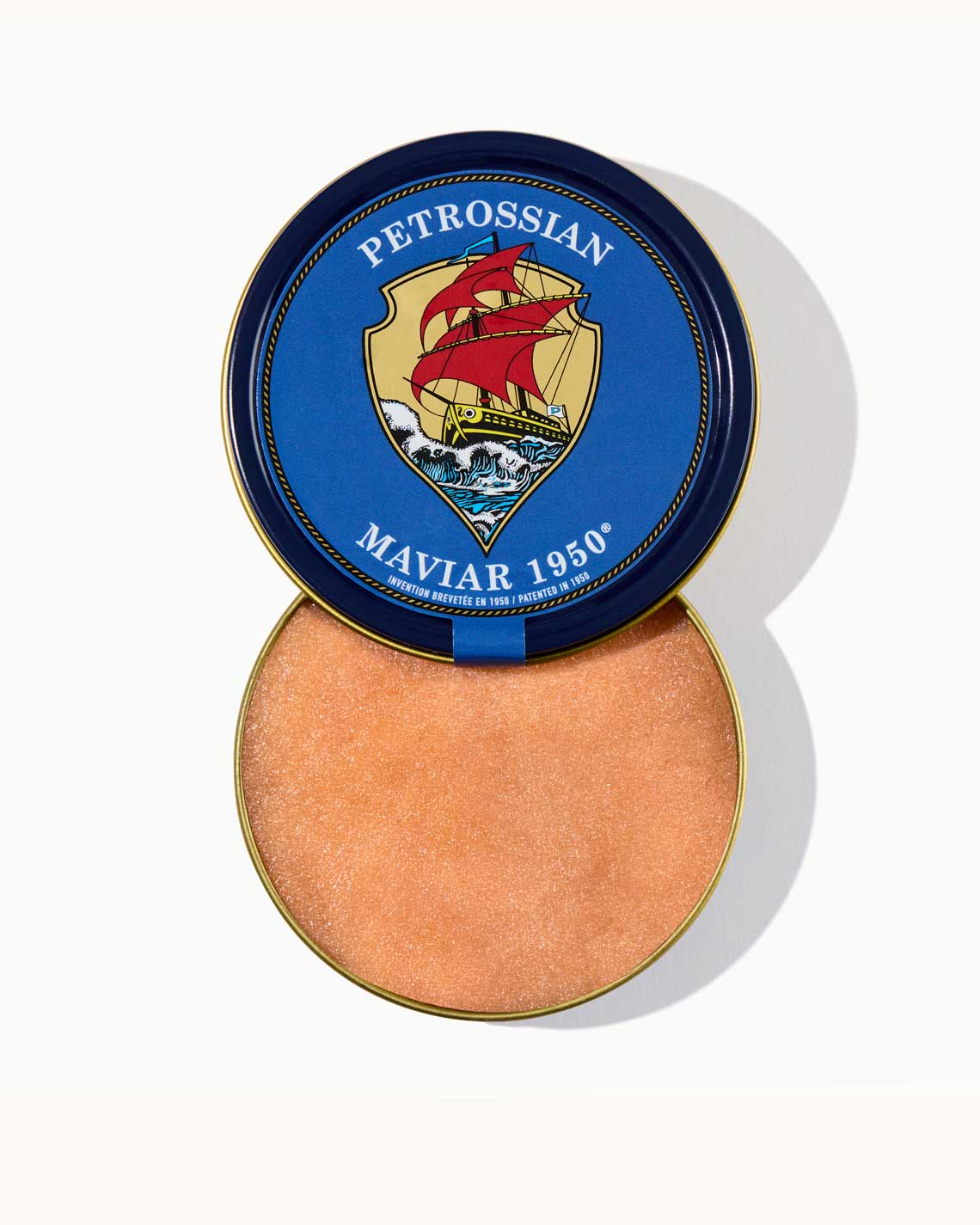 an overhead shot of blue metal tin with an vintage Petrossian logo, opened to reveal it is filled with pink, smooth maviar eggs.