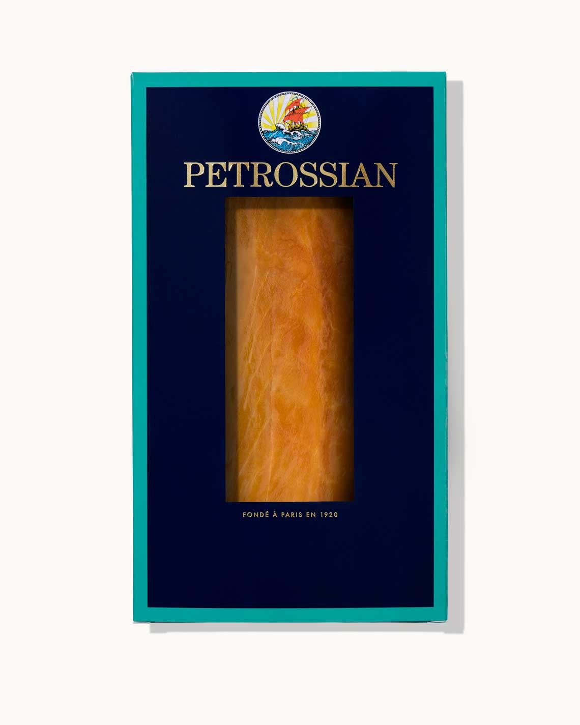 A navy blue Petrossian box with teal trim sits on a white background. A juicy filet of cold-smoked trout can be seen through a cut-out in the center of the box.