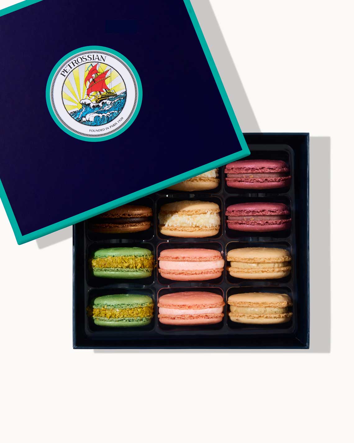 a navy blue Petrossian box with teal trim, filled with a dozen crisp, creamy french macarons of different pastel colors.