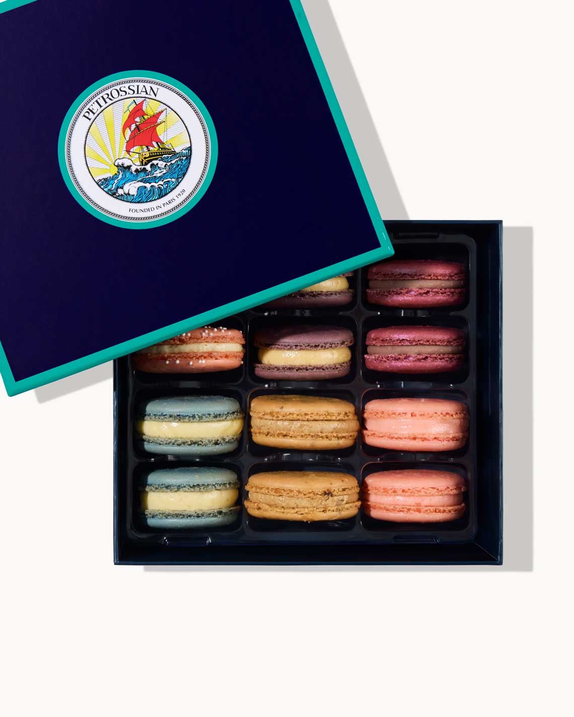 a navy blue Petrossian box with teal trim, filled with a dozen crisp, creamy french macarons of different pastel colors.