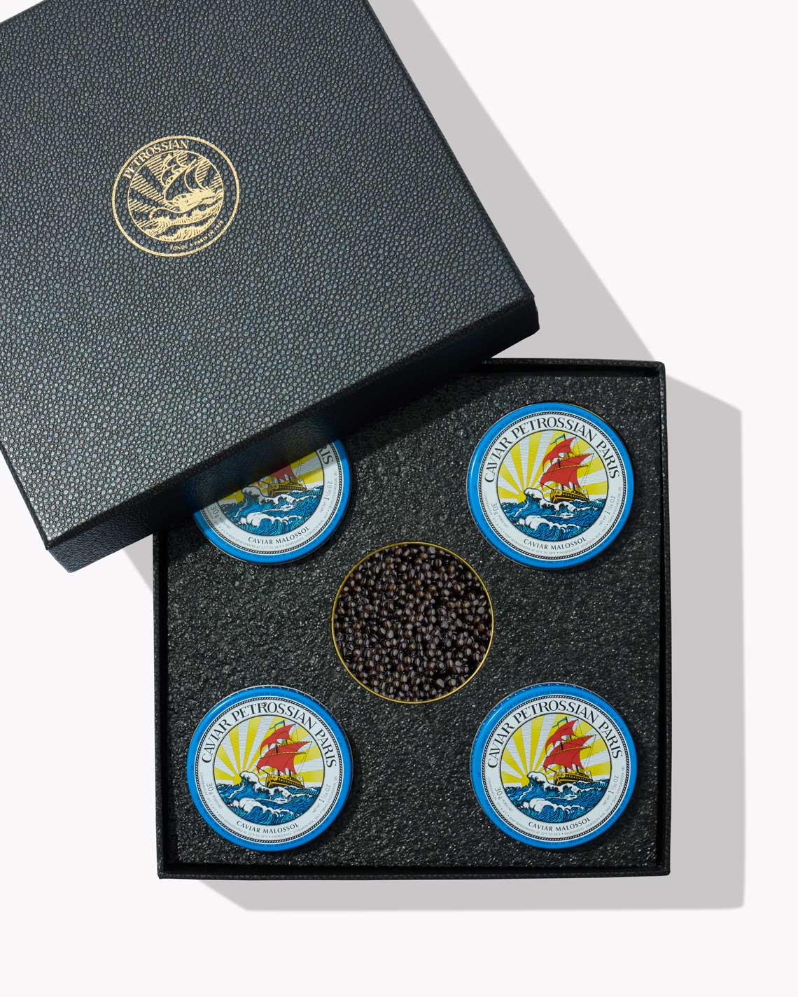 five tins of caviar, including one that is open, sit comfortably in a black textured box, baring a golden Petrossian logo.
