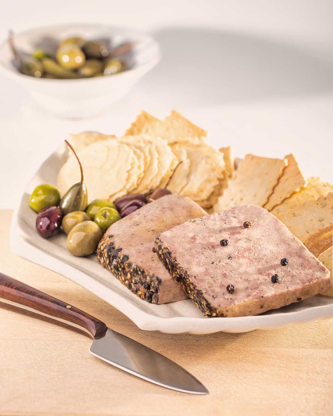 a loaf of delicious pepper pate, sliced and plates with light crackers and olives