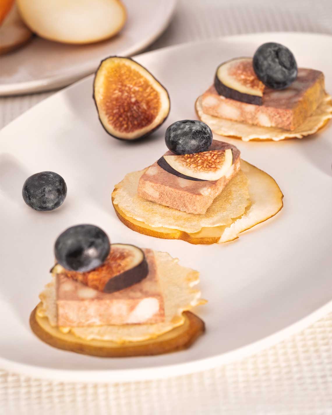 slices of brandy pate plated on pear slices with blueberries and figs