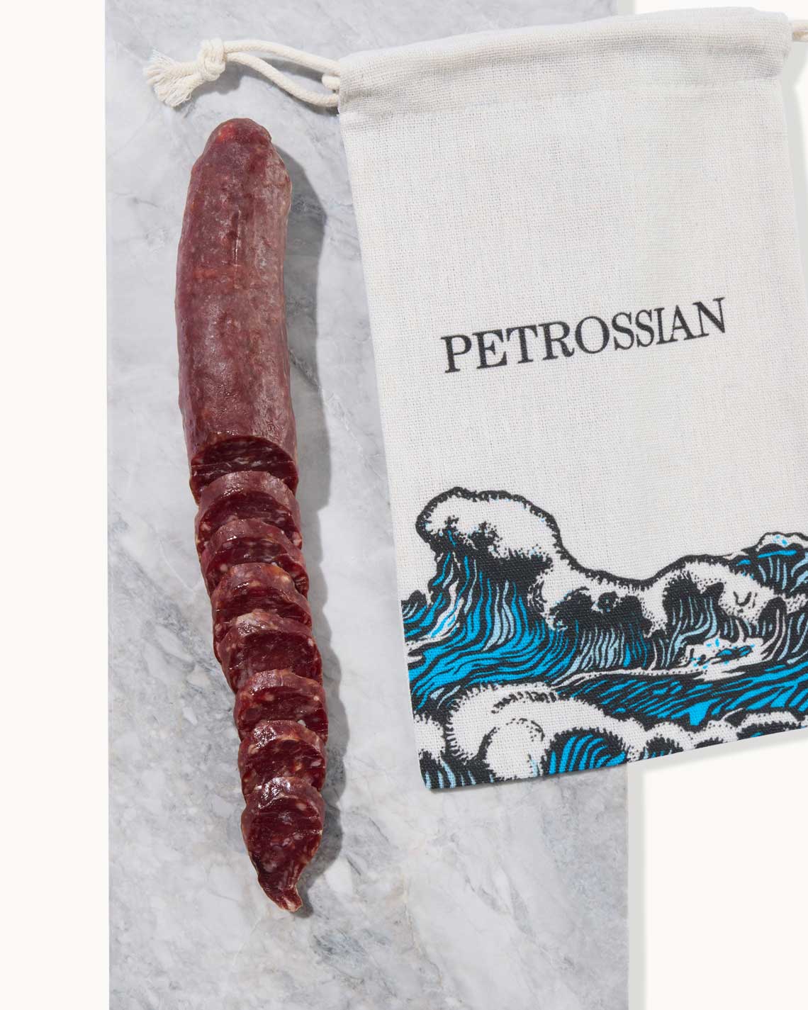 a dark red marbled cured saucisson, partially sliced and placed on a marble slab with a Petrossian white bag