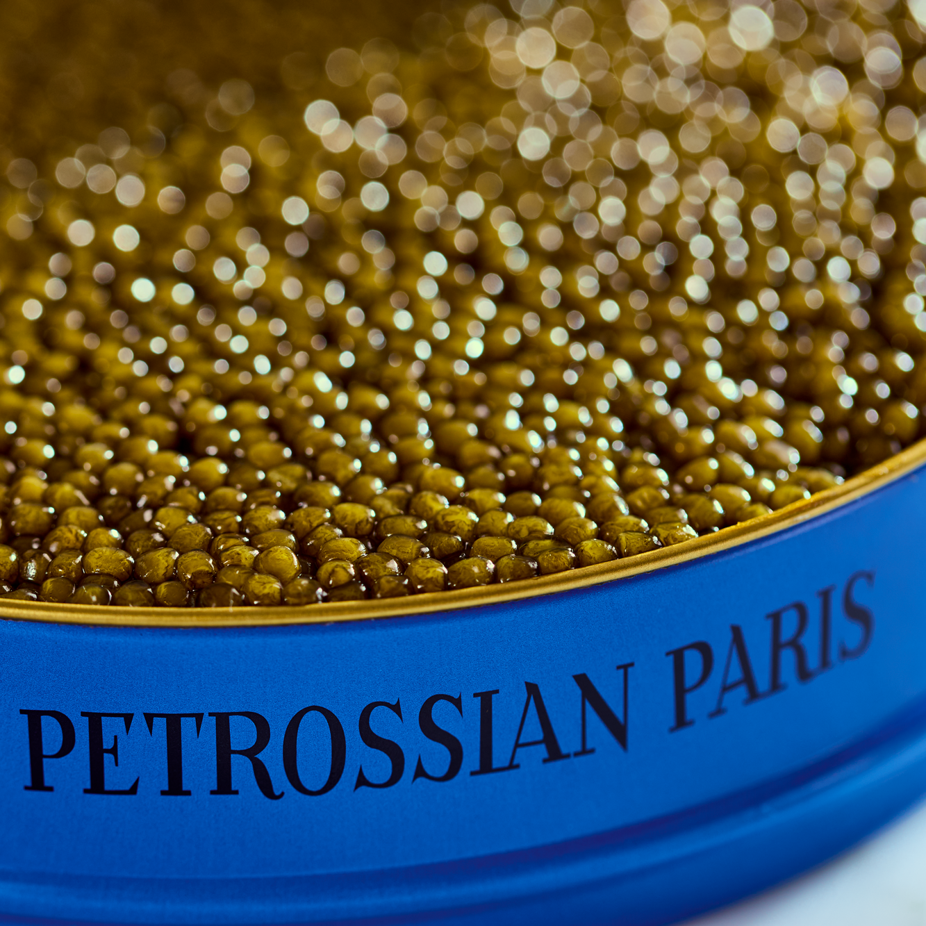 golden beads of Kaluga-Huso caviar sits in a deep blue Petrossian tin. The light is very dramatic and reflects brilliantly off the caviar. 