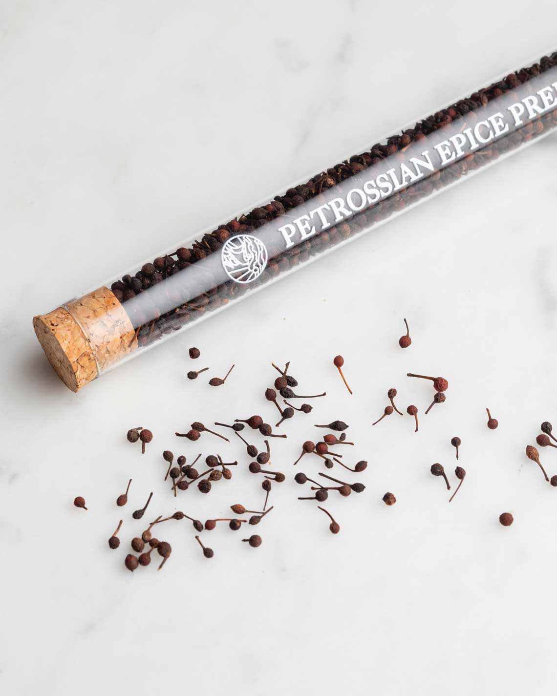 a glass vial with a cork, filled with small black peppercorns with more peppercorns spread out on a marble slab