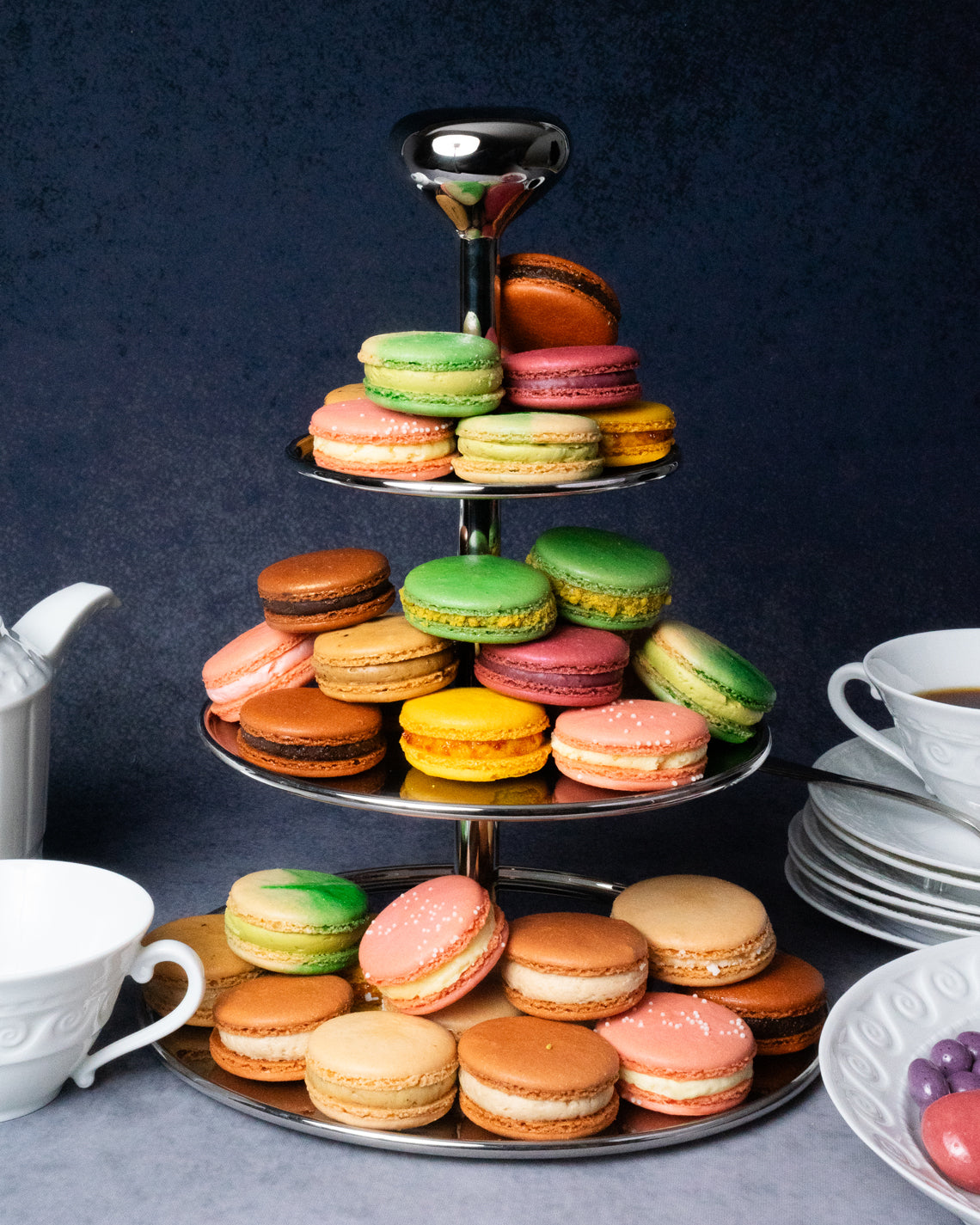 an incredible three-tiered tower of a colorful french macarons, in front of a purple background. the macarons st happily together and range in color from hot pink to dark brown