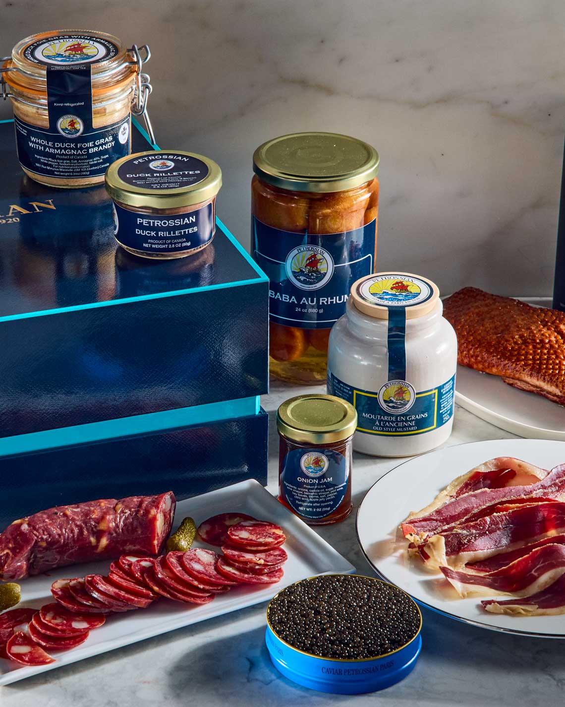 a collection of Petrossian delicacies arranged on a white marble counter, including a tin of caviar, charcuterie and jars of foie gras.