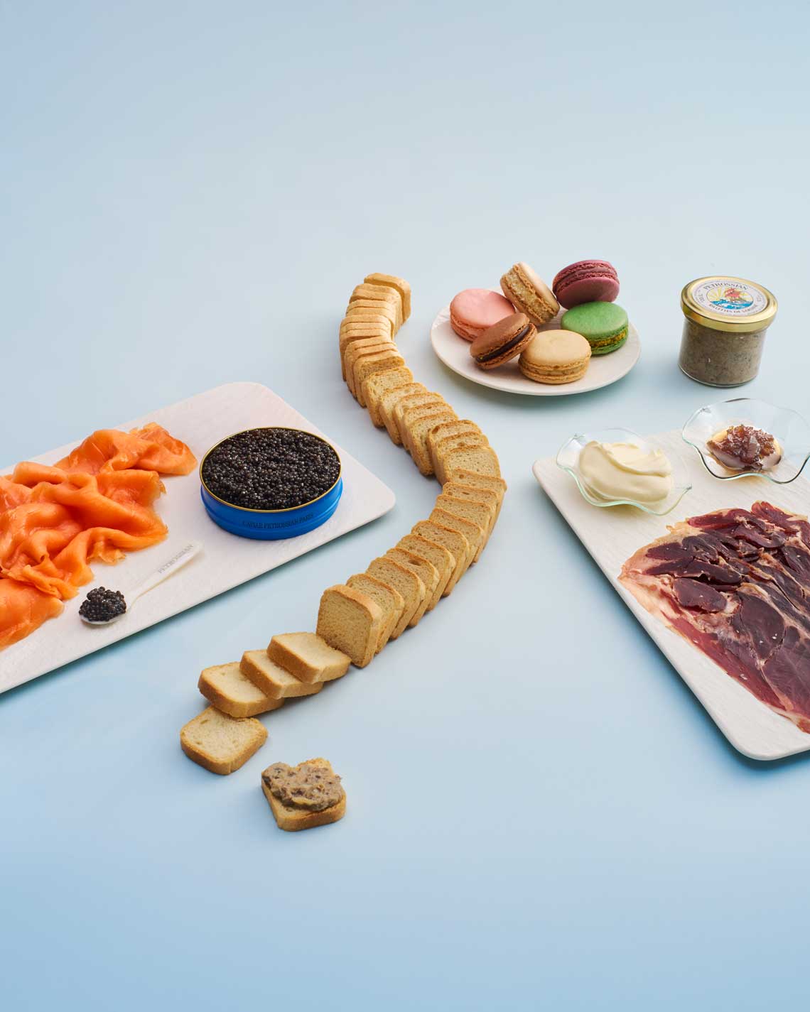 Assorted food items including cured meats, bread, caviar and pastries on a light blue background