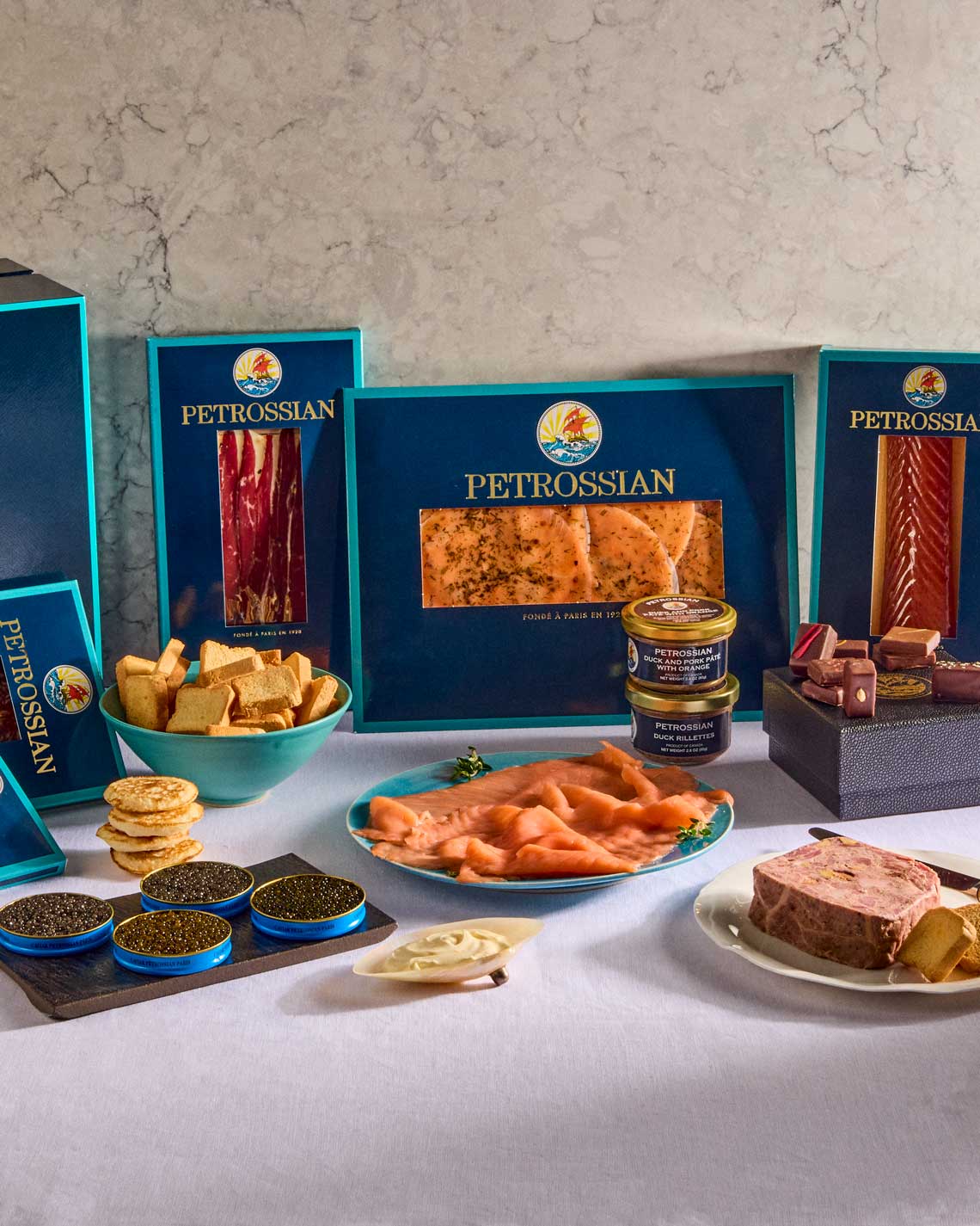 the delicious contents of the gift basket, laid out on a marble countertop with a navy blue and teal Petrossian gift box