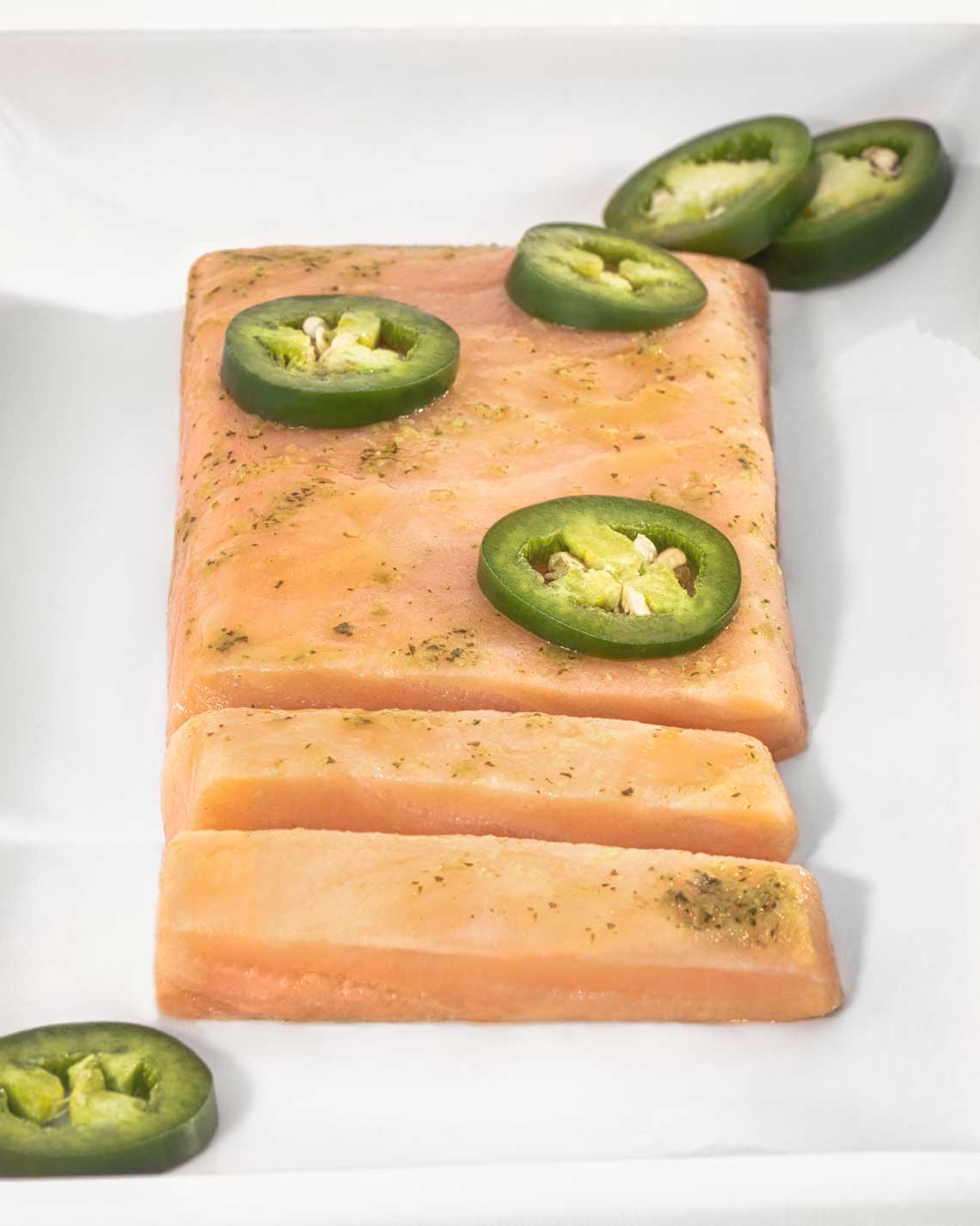 a generous filet of vibrant partially-sliced orange smoked salmon on a white plate, topped with thick jalapeno slices