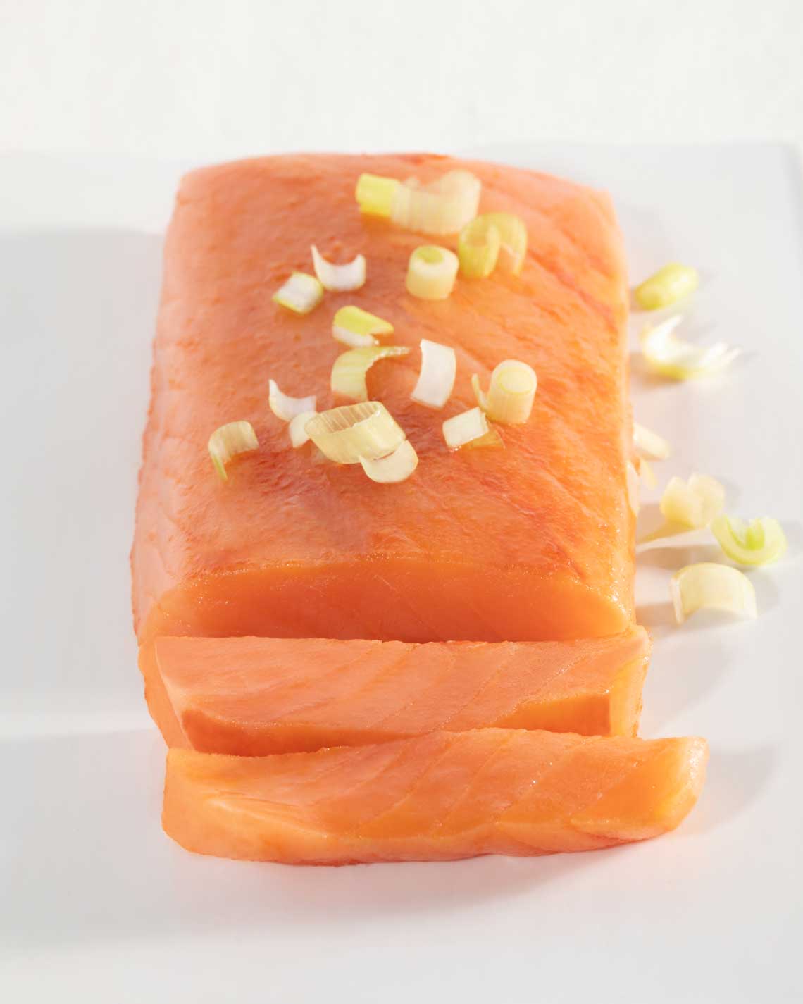 a generous filet of vibrant partially-sliced orange smoked salmon on a white plate, topped with slices of chives