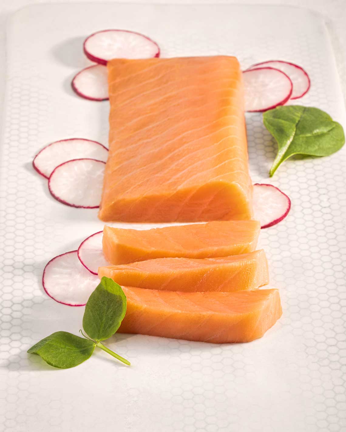 a generous filet of vibrant partially-sliced orange smoked salmon on a white plate, topped with light greenery and garnished with radish slices