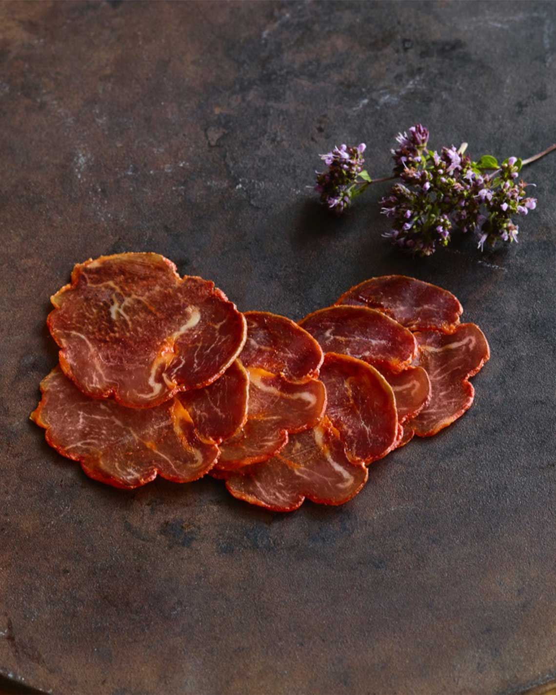 thick, red slices of Spanish pork loin, laid out on stone slab with violet flowers