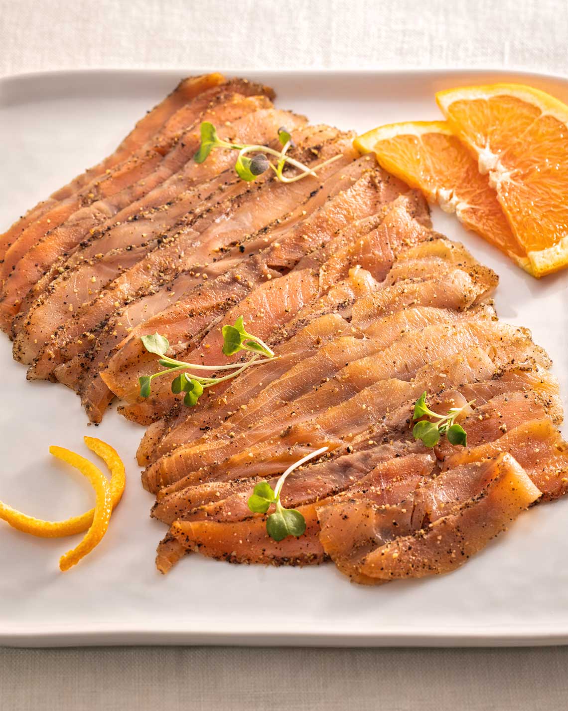 luscious slices of pastrami trout laid out on a white plate with orange slices