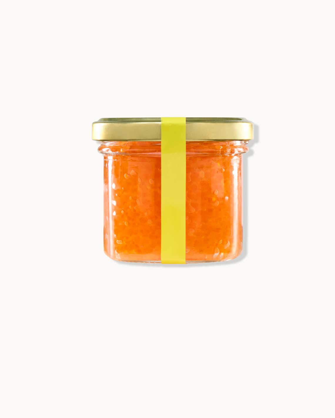 a glass jar with a copper lid and yellow label, filled with bight orange beads of Petrossian trout roe sitting on a white background