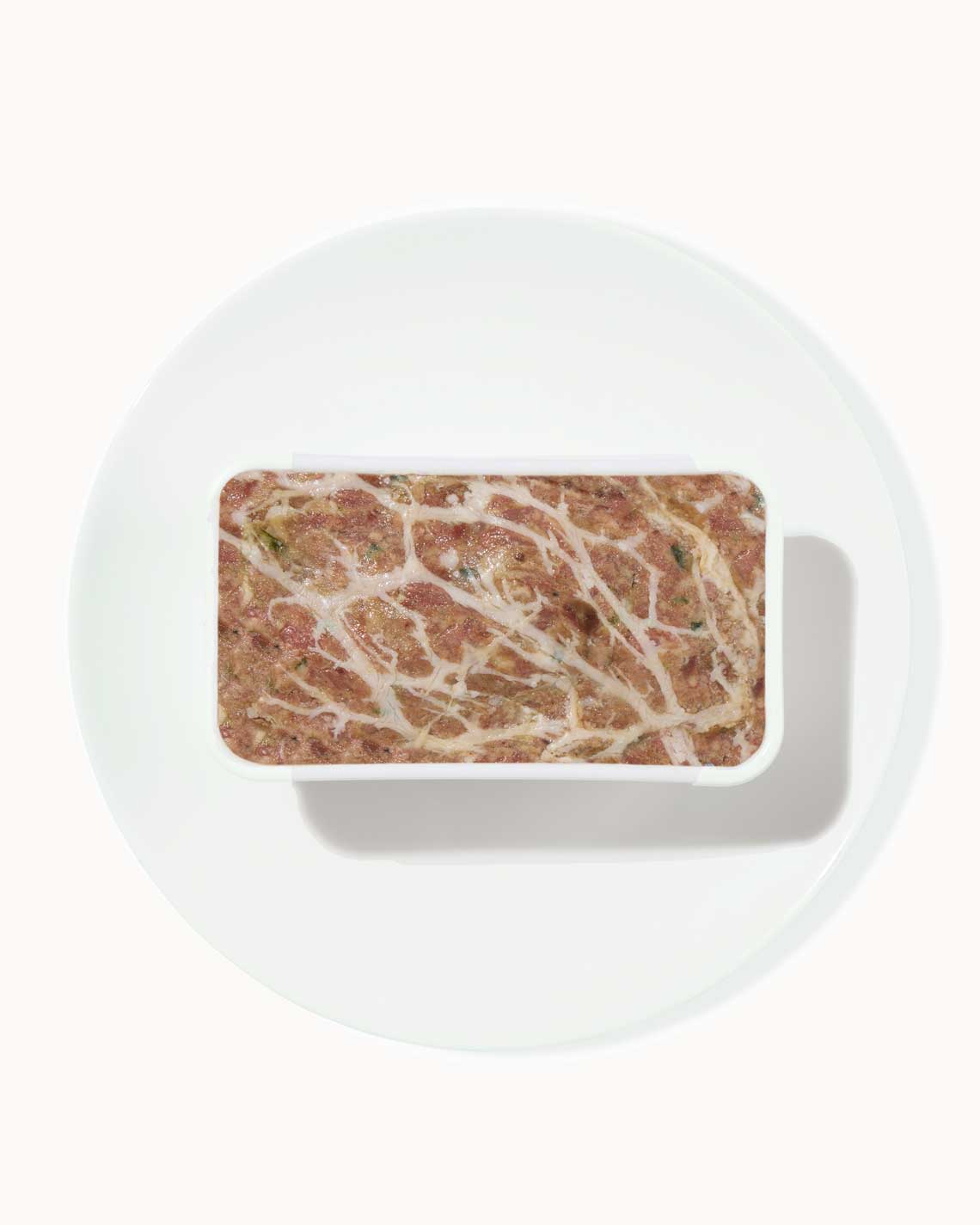 a terrine of rich, succulent pâté sits on a white plate on a white background.