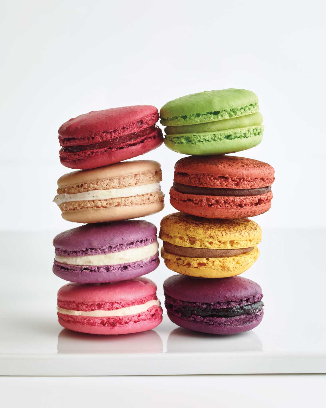 two stacks of four brightly-colored macarons stand together on a polished white countertop. 