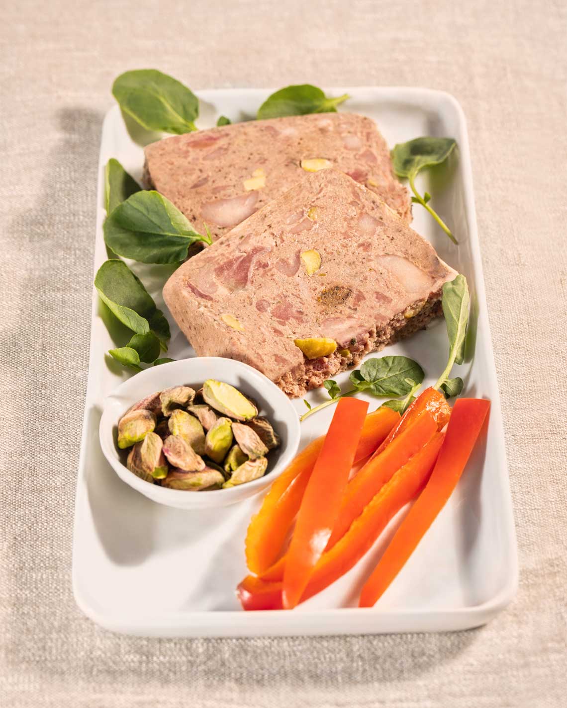 a sliced loaf of pheasant pate, plated with orange peppers and pistachios and garnish