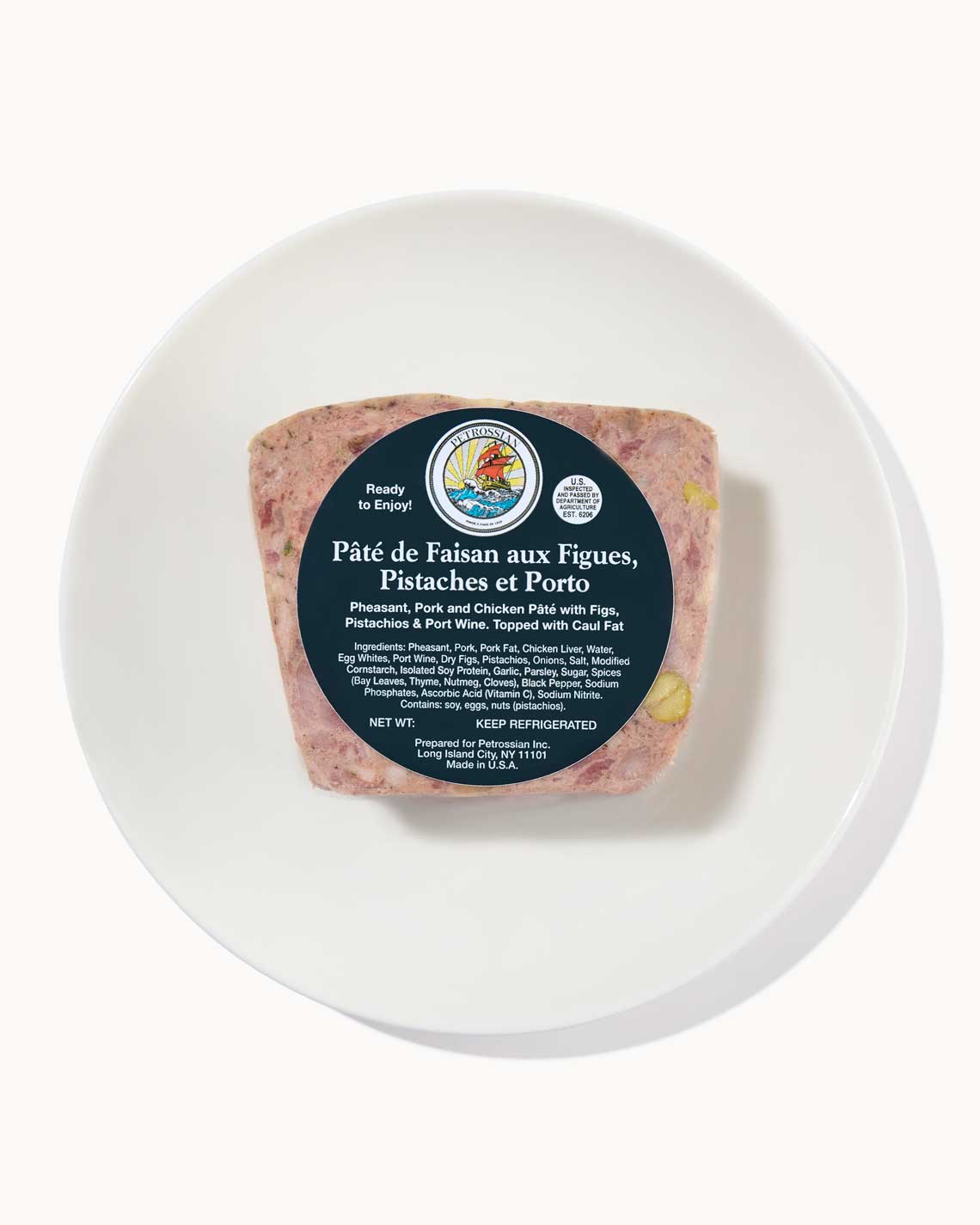 a healthy loaf of Pheasant pate speckled with nuts and wrapped with a blue Petrossian label on a white plate 