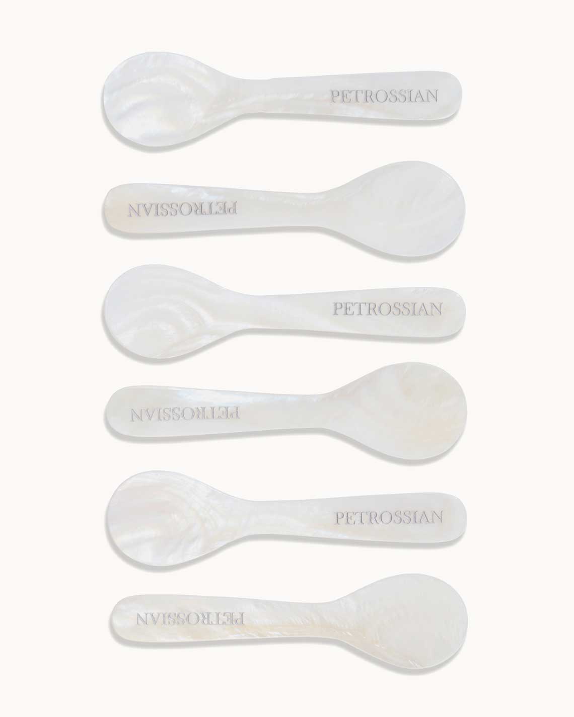 six pearl spoons are carefully arranged next to each other on a white background. each has "Petrossian" engraved on the handle.