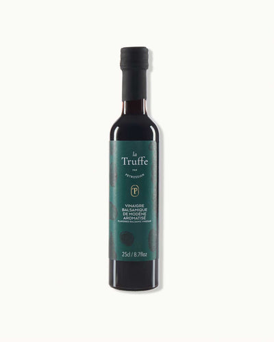 a tall glass bottle with a dark green "la Truffe" label lies on a white background. it is filled with rich dark balsamic vinegar.