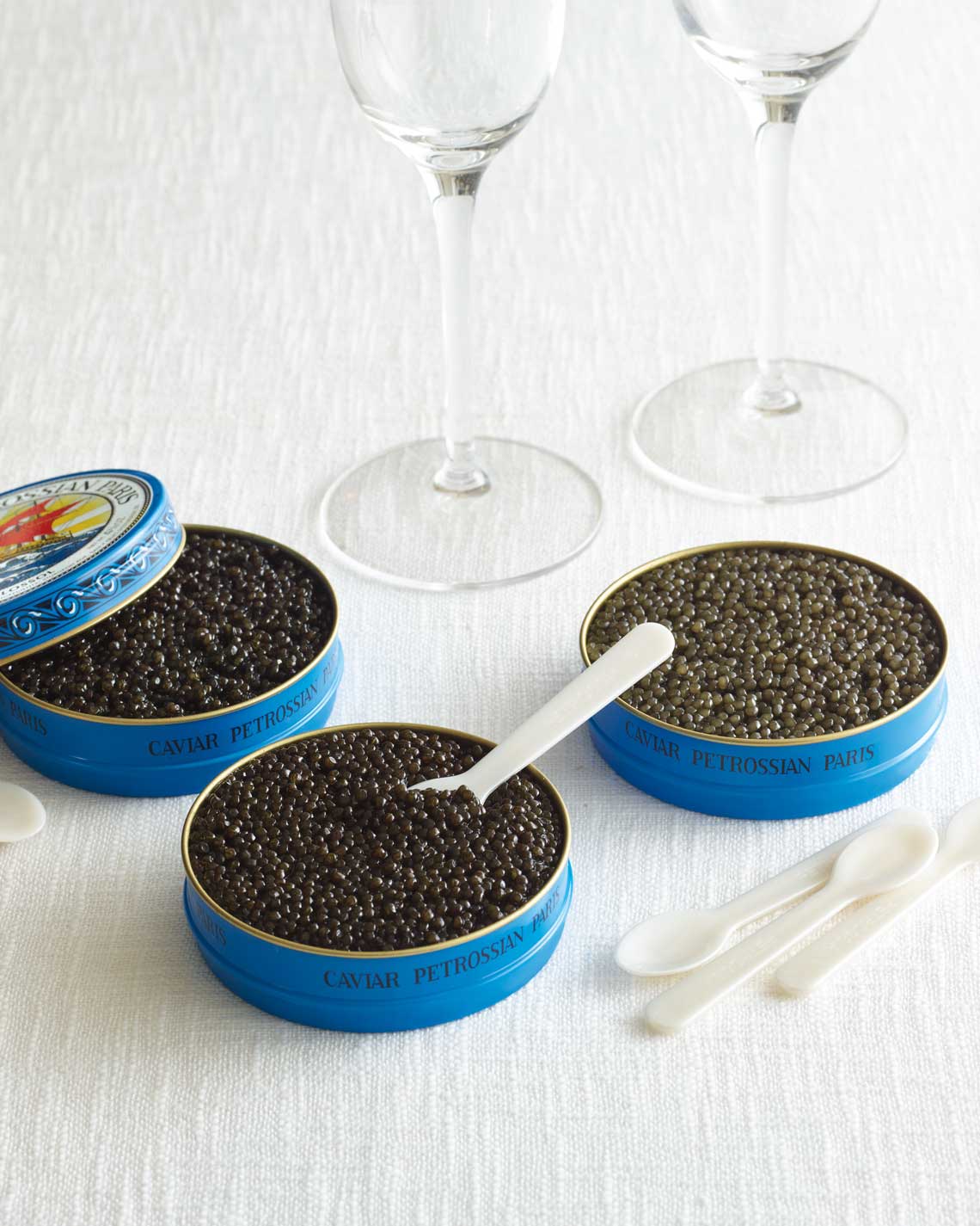 Three large tins of delicious caviar with pearl spoons and wine glasses on a linen cloth