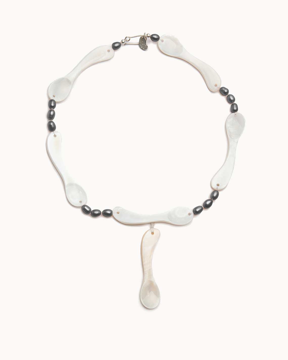 a circular necklace made of light cream-colored mother-of-pearl spoons lies on a flat white background. They are connected by tiny onyx beads.