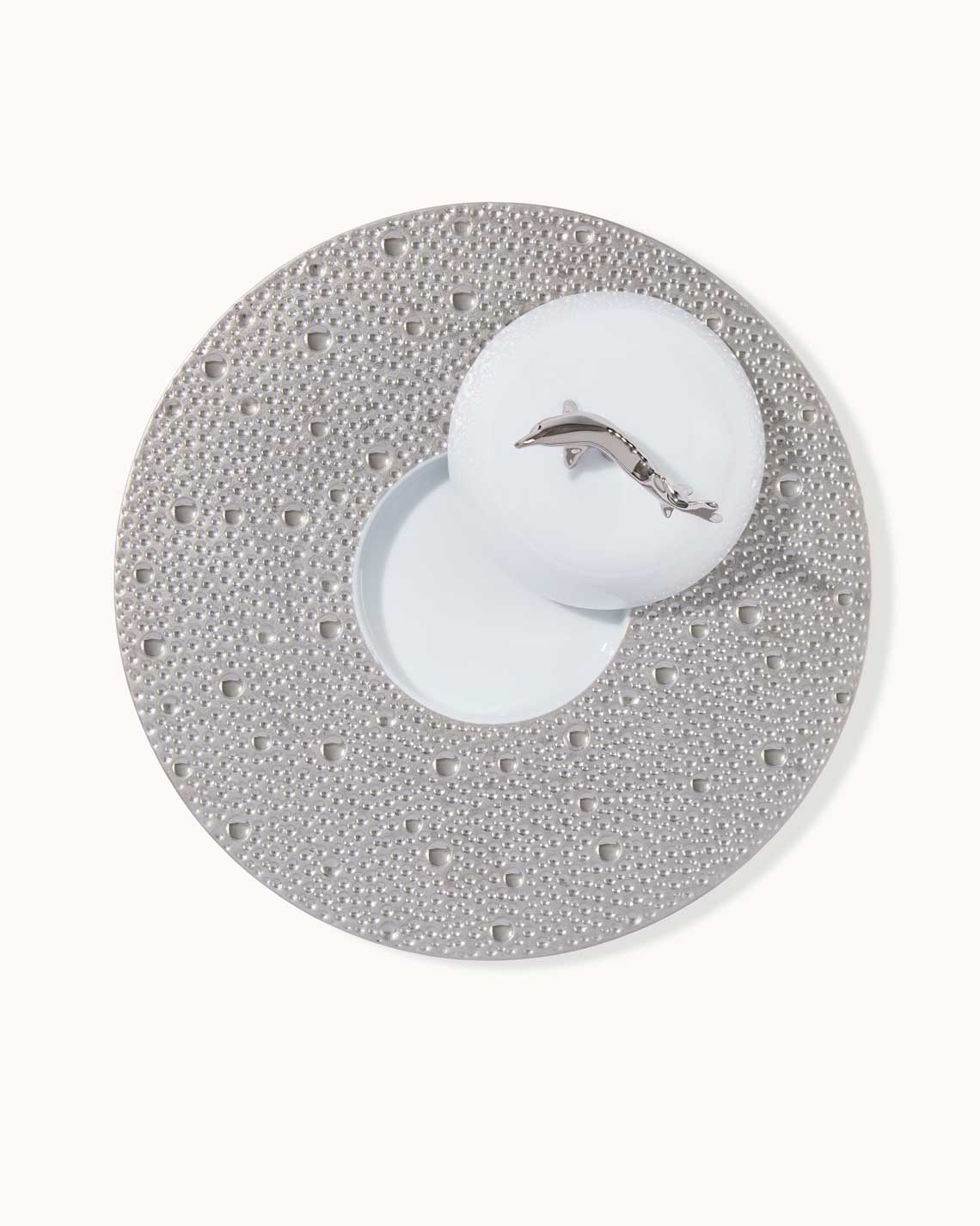 a platinum bubble-pattern plate with a place for a caviar tin and an ecume lid topped with a platinum sturgeon