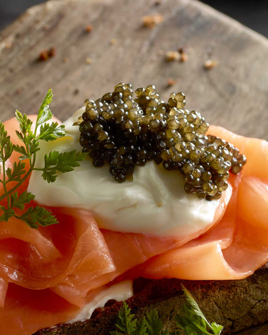 A close-up of a dollop of jade caviar, sitting onto of a pat of creme fraiche and a ribbons of luscious smoked salmon over a thick slice of bread.